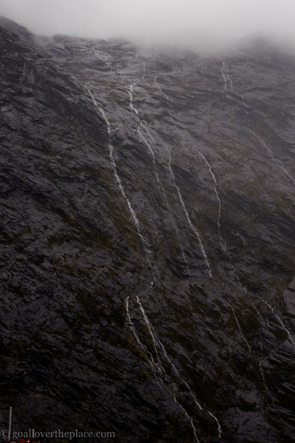 trails of waterfalls down the face of a black cliff in Fjordland National Park, New Zealand