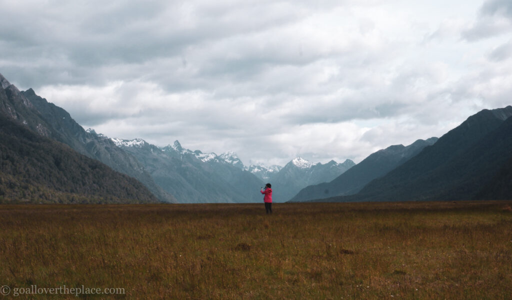 a woman in a red coat stands between two cliffs in Fjordland, New Zealand