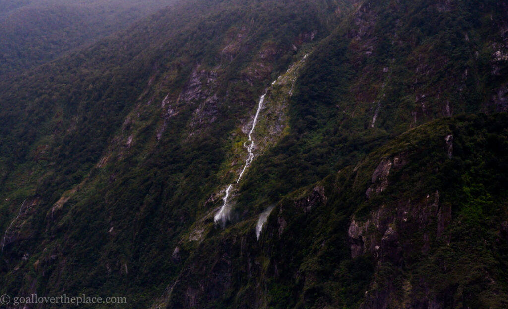half of a waterfall cascades down a cliff in Fjordland National Park, New Zealand