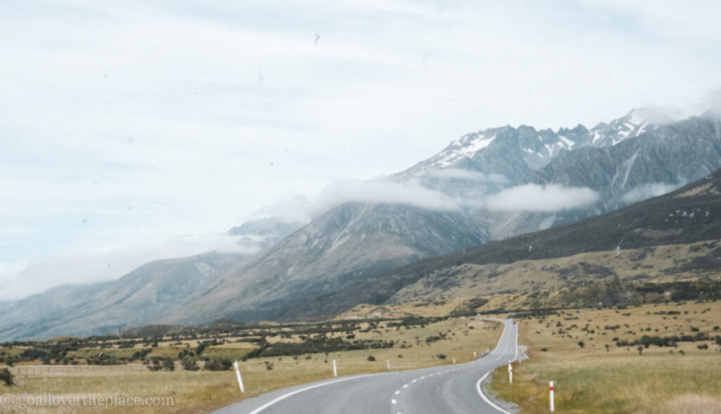 a road stretches out front underneath a cloud-covered mountain in South Island, New Zealand